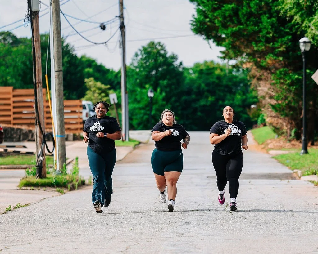 Three clients jogging on a street outside of the gym, wearing matching black PowerHouse t-shirts, with trees and street lamps in the background.