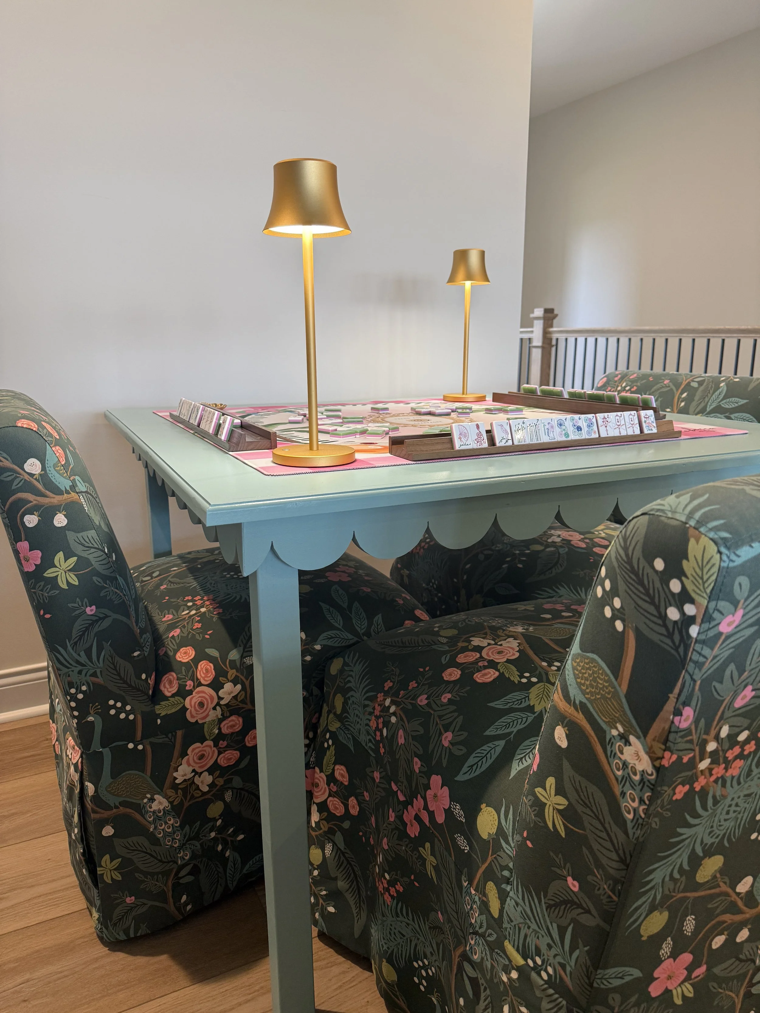 Handcrafted custom painted mahjong table with scalloped edges by The Mahj Table Co featuring a floral table mat, elegant seating, and a stylish game night setup