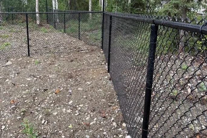 Cleared and leveled area along a chain-link fence after brush and vegetation removal.