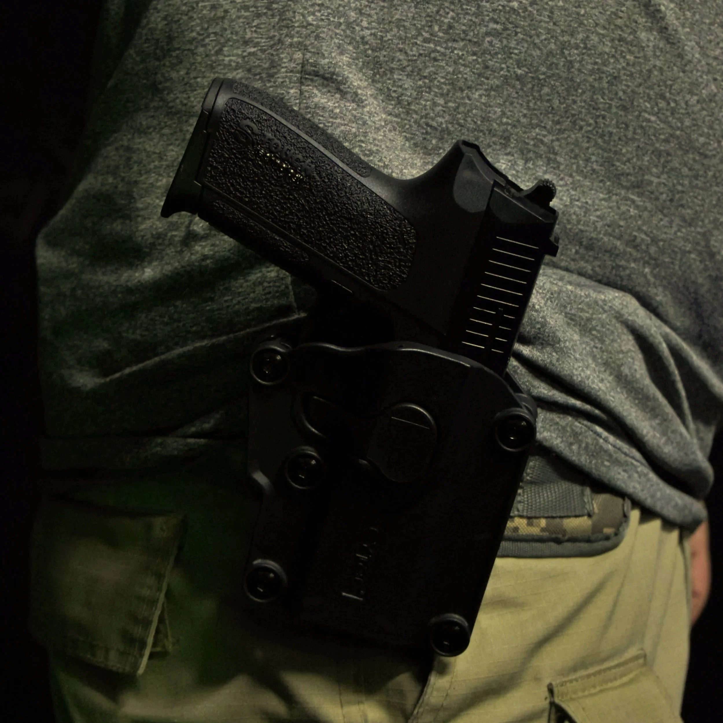 A black firearm with a textured grip and a scope mounted on top, placed against a dark, textured surface.