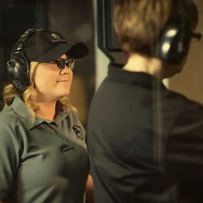 A woman with sunglasses and headphones in a recording studio, facing another person with headphones, both involved in a recording session.