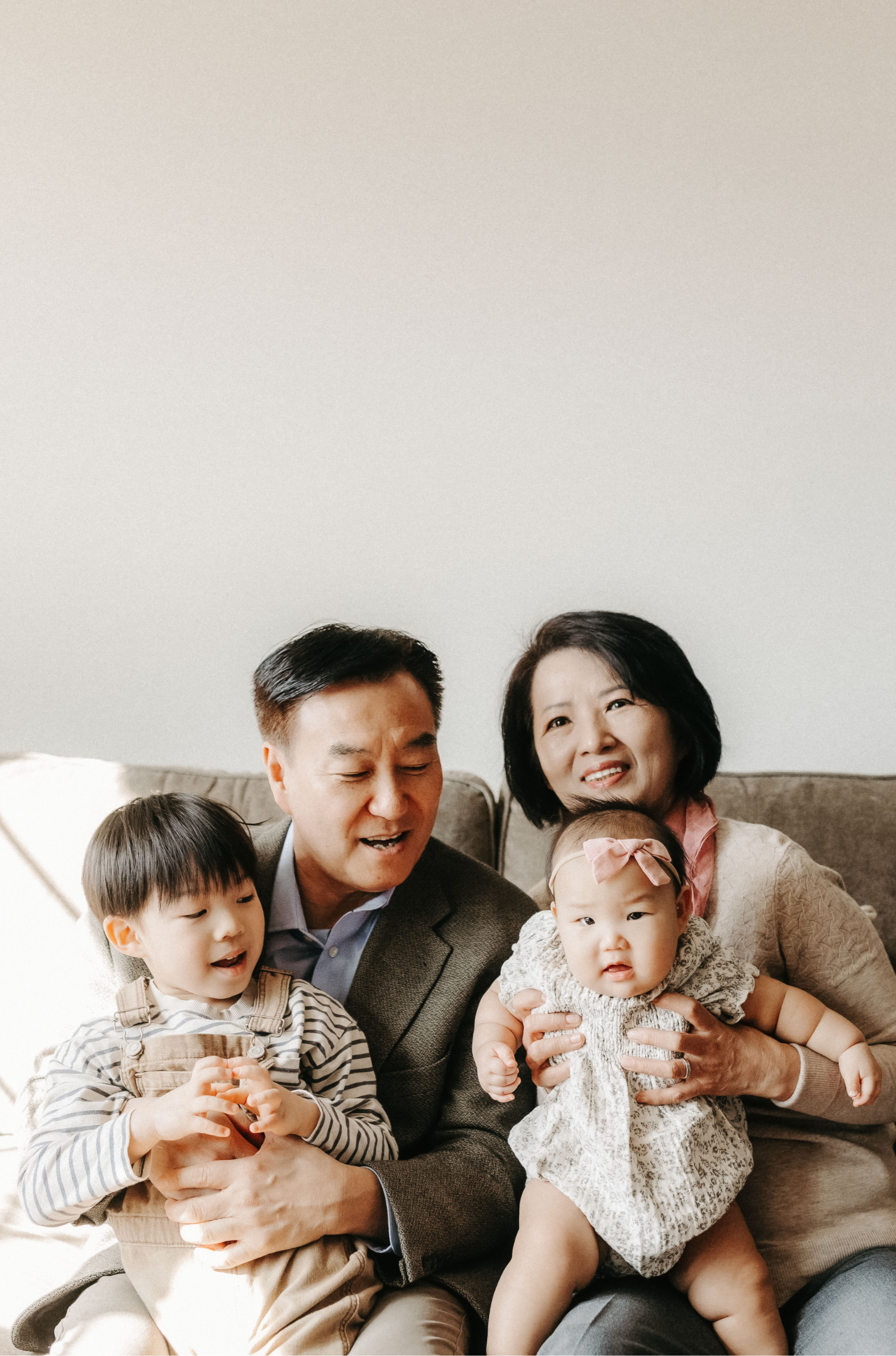 A multigeneration Asian family celebrating together indoors, with parents, children, and a baby, smiling and holding each other.