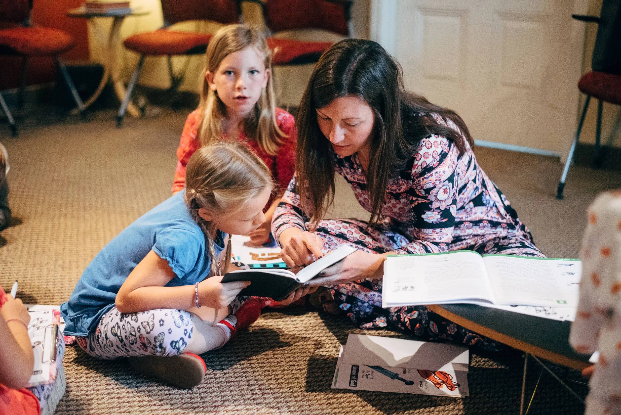 A teacher reads a Bible storybook with three young girls seated on the floor during Sunday School