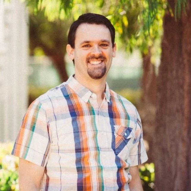 Bret Rooks, Worship Director and elder, smiling outdoors in a plaid shirt