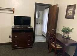 Room with a dresser and a small television on top, a door slightly open leading to a bathroom, and a desk with a plant and a chair.