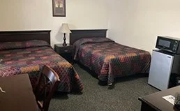 A hotel room with two beds, a nightstand with a lamp, and a mini refrigerator with a microwave on top.
