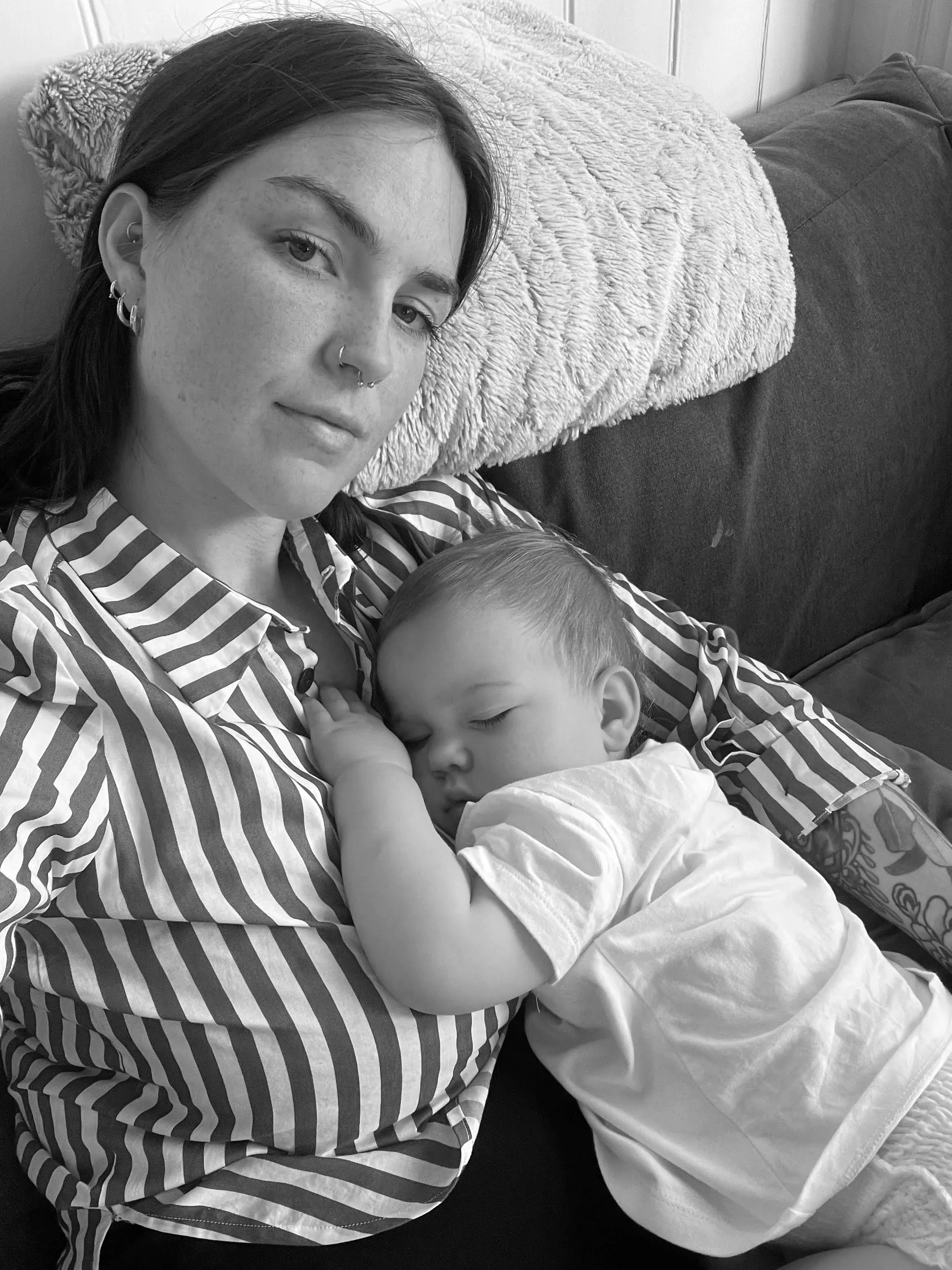 Black and white image of Carli and her baby. Carli wears a striped shirt and is sitting on a couch