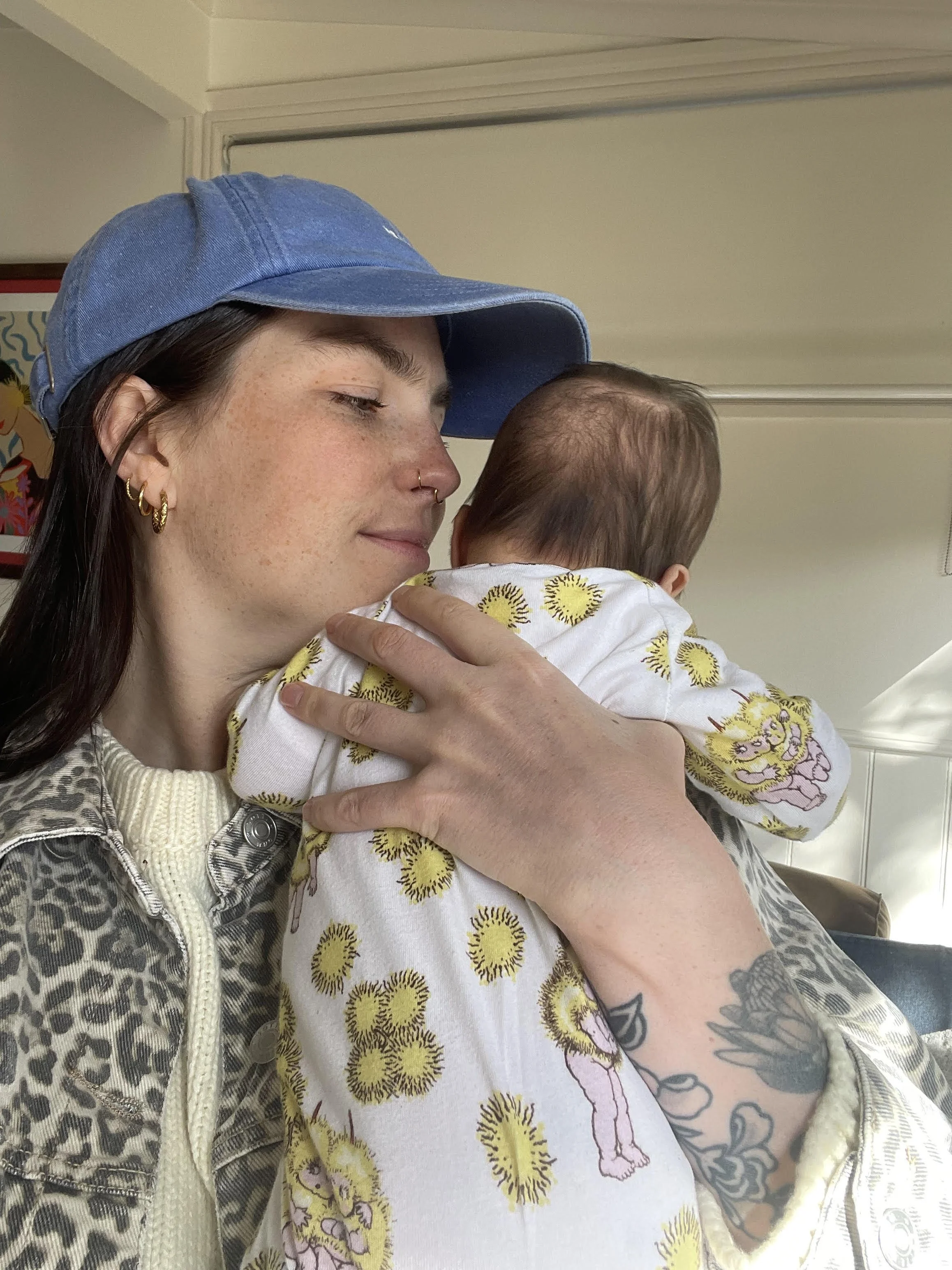 Carli wearing a blue cap and leopard bring jacket holding a baby wearing a gumnut baby onesie