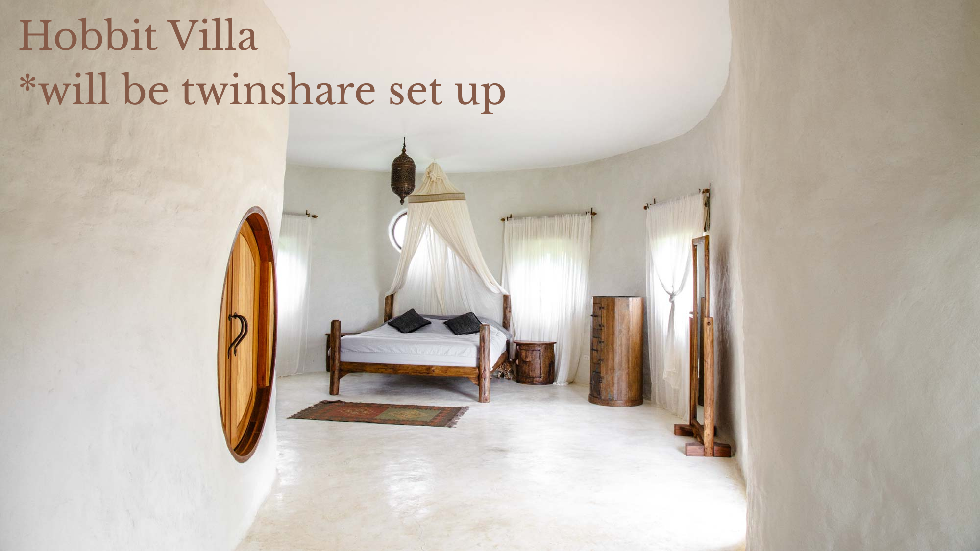 A cozy bedroom with white textured walls and ceiling, featuring a castle-style wooden bed with white linens and black pillows, surrounded by rustic wooden furniture including a small dresser and a stool, illuminated by natural light from tall windows