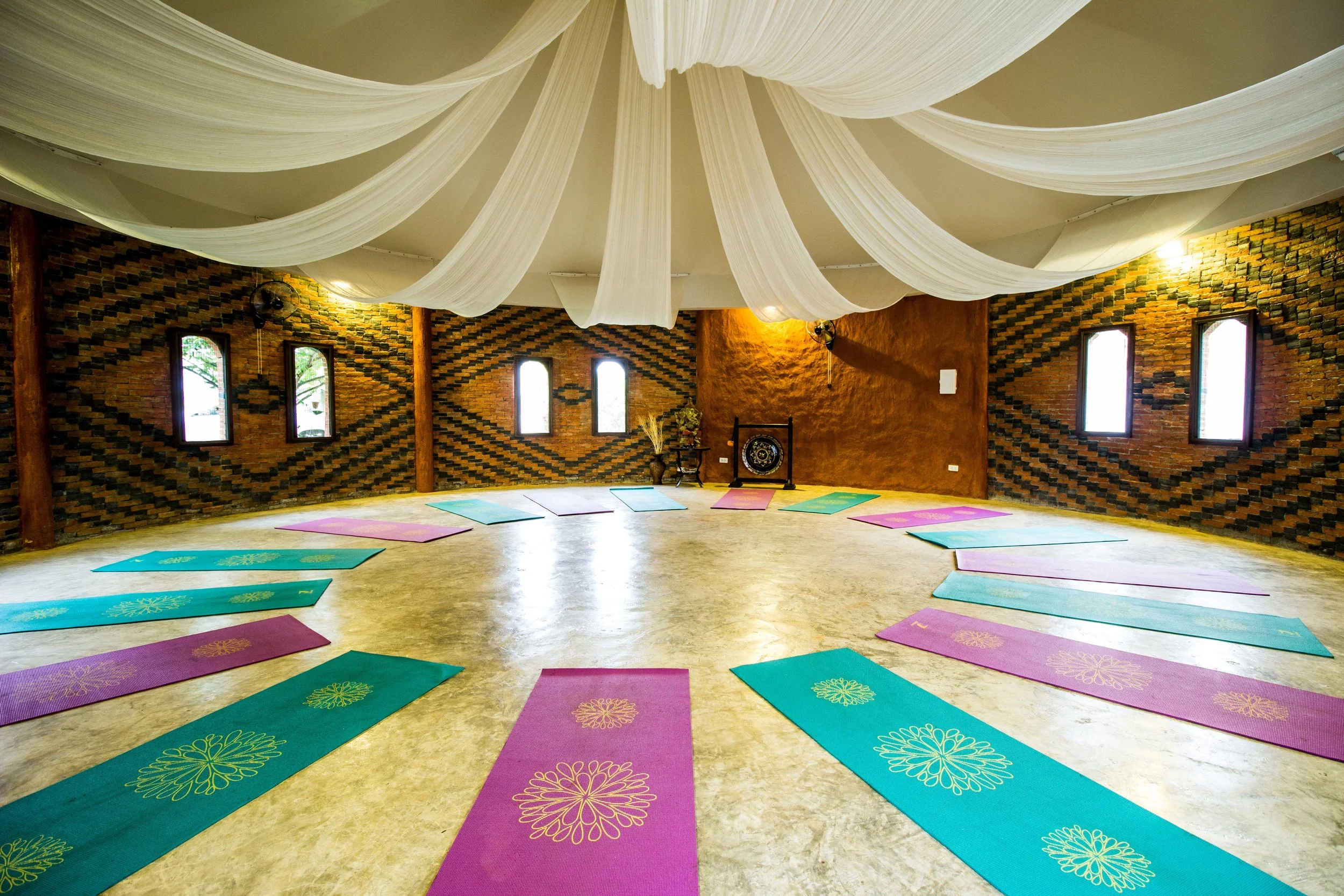 A yoga or meditation room with colorful mats arranged in a circle, brick walls, and white fabric draped on the ceiling.