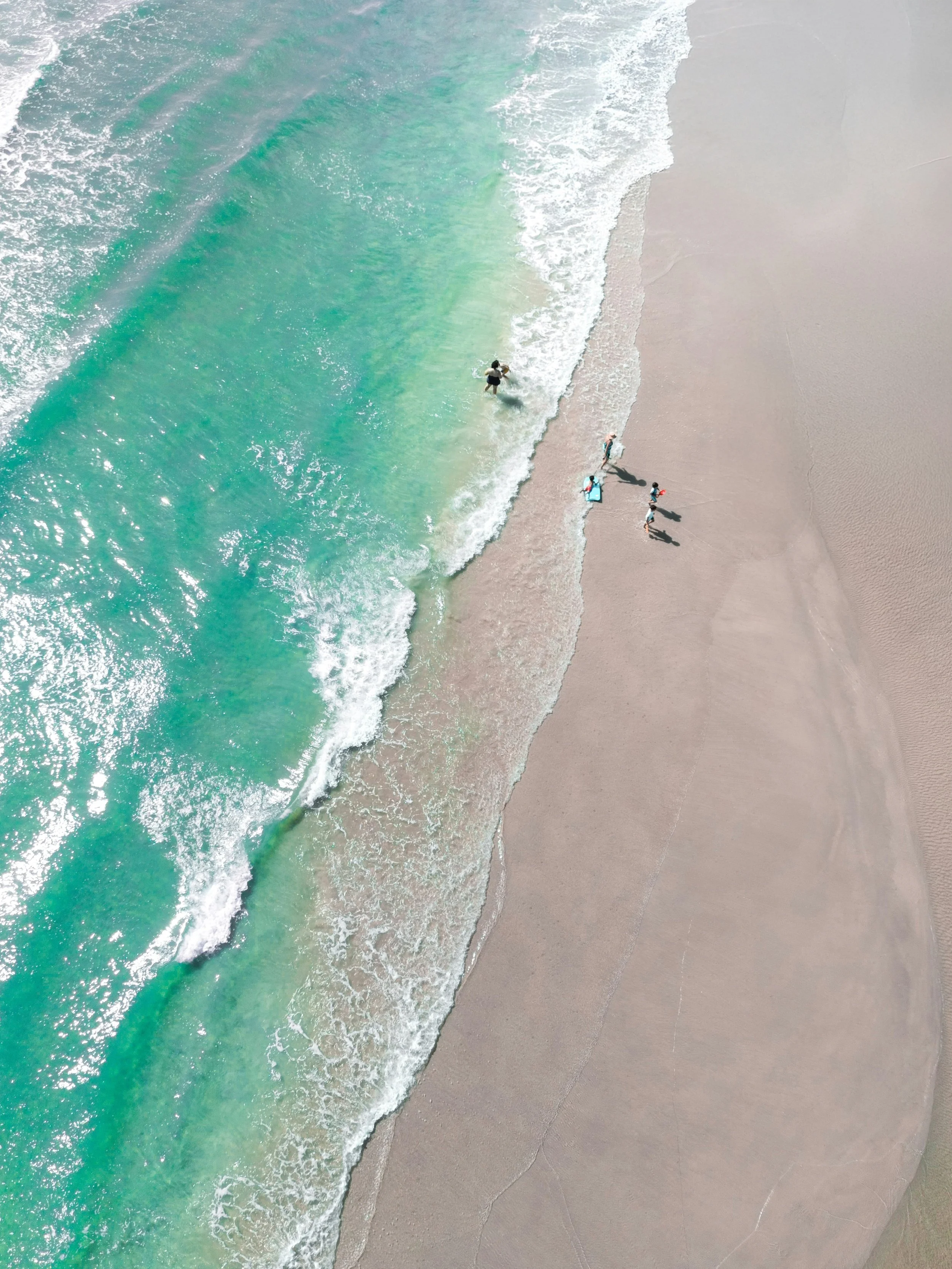 Bird's-eye view of a sandy beach with turquoise ocean waves and a small group of people walking along the shoreline.