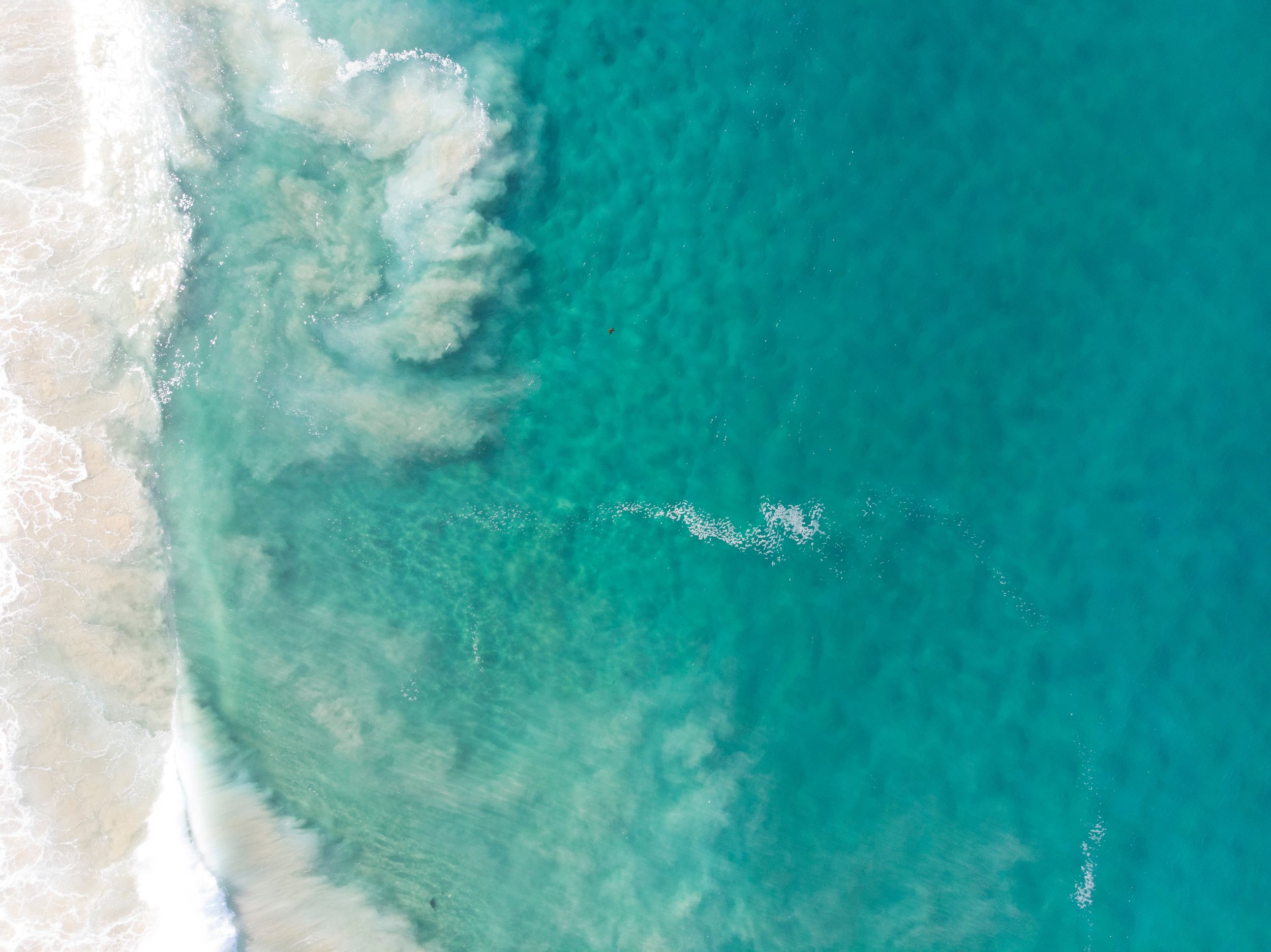 Aerial view of turquoise ocean waves crashing onto a sandy beach.