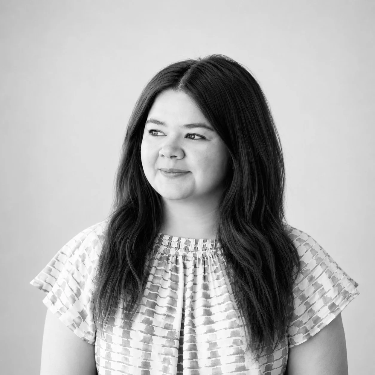 Black and white portrait of a woman with long dark hair, wearing a patterned top, looking slightly to her left with a calm expression.