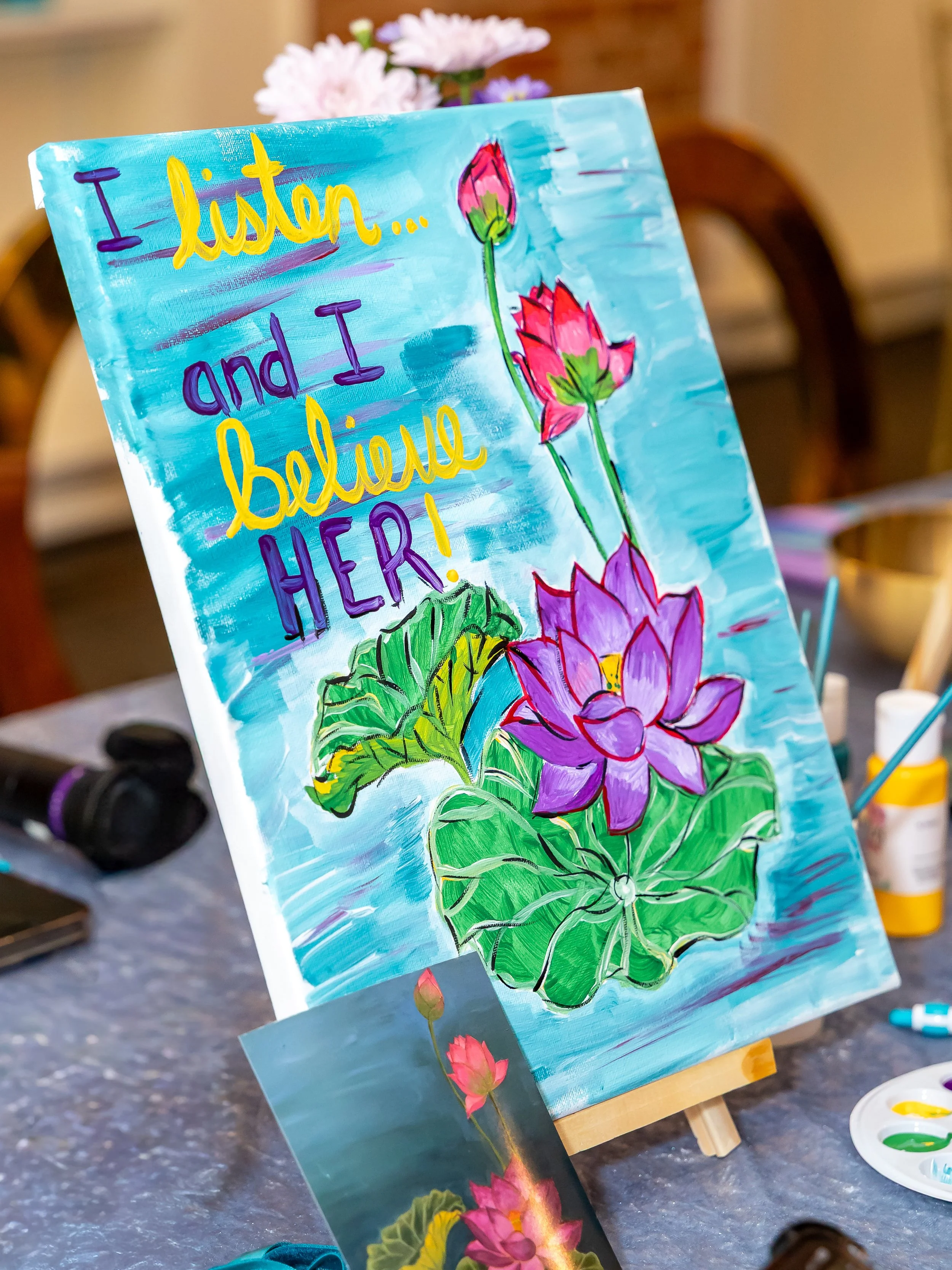 Painted canvas with colorful flowers and the quote, 'I listen... and I believe HER!'