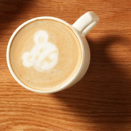 A white coffee mug on a wooden surface with latte art resembling a smiley face.