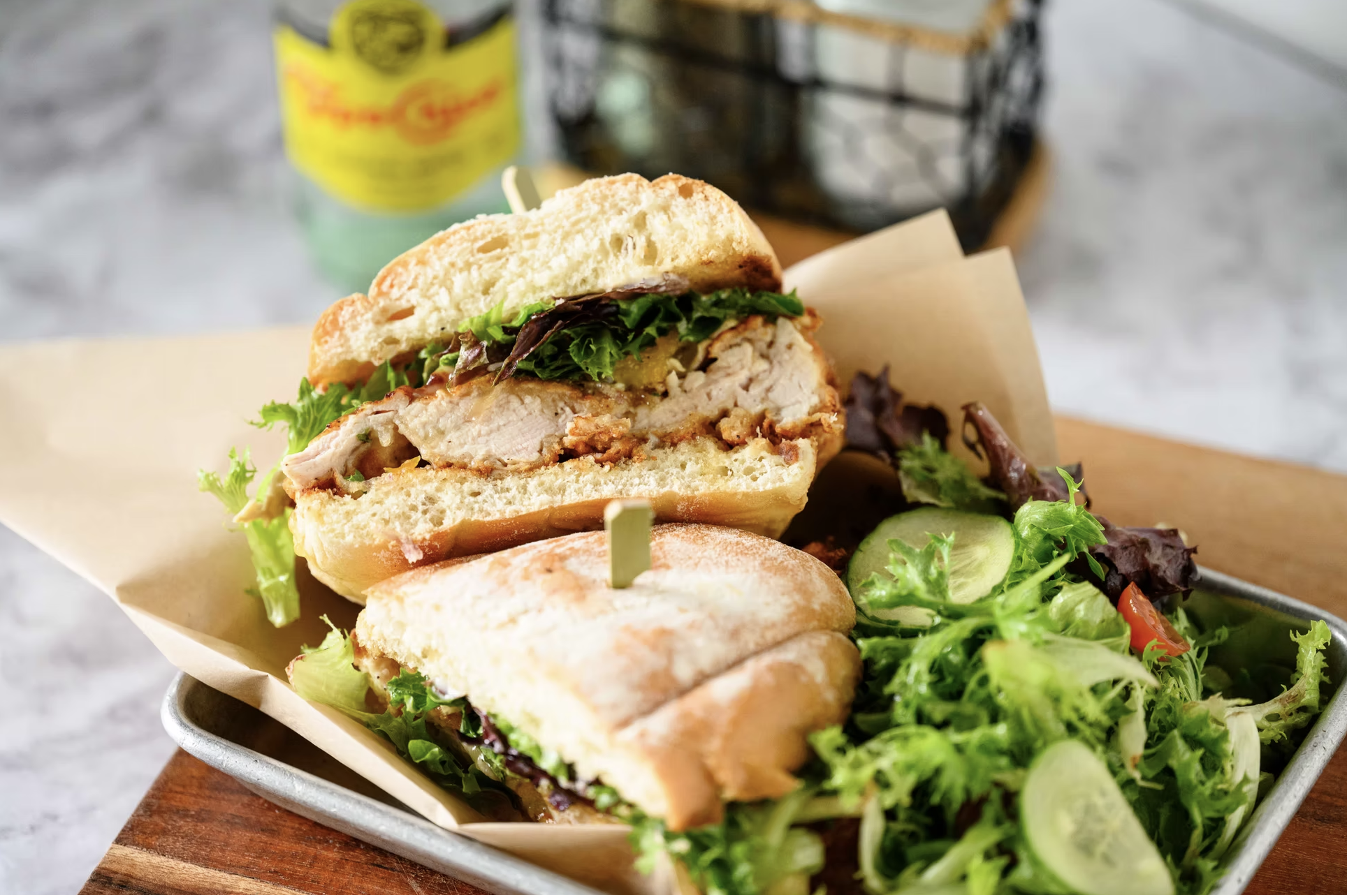 Close-up of a grilled chicken sandwich with lettuce and pickles in a sandwich bun, served with side salad greens.
