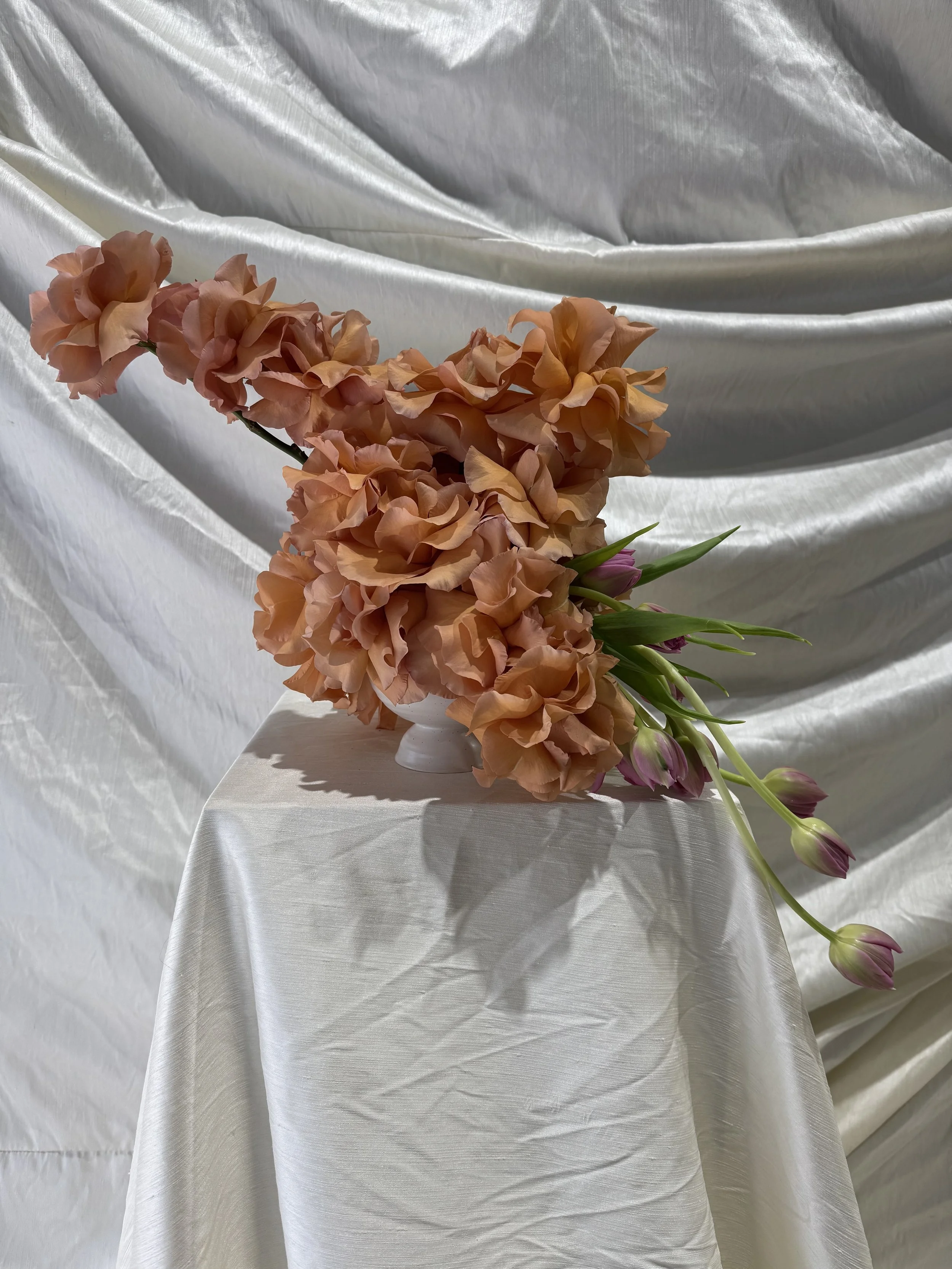 A bouquet of peach-colored flowers on a white satin cloth background.