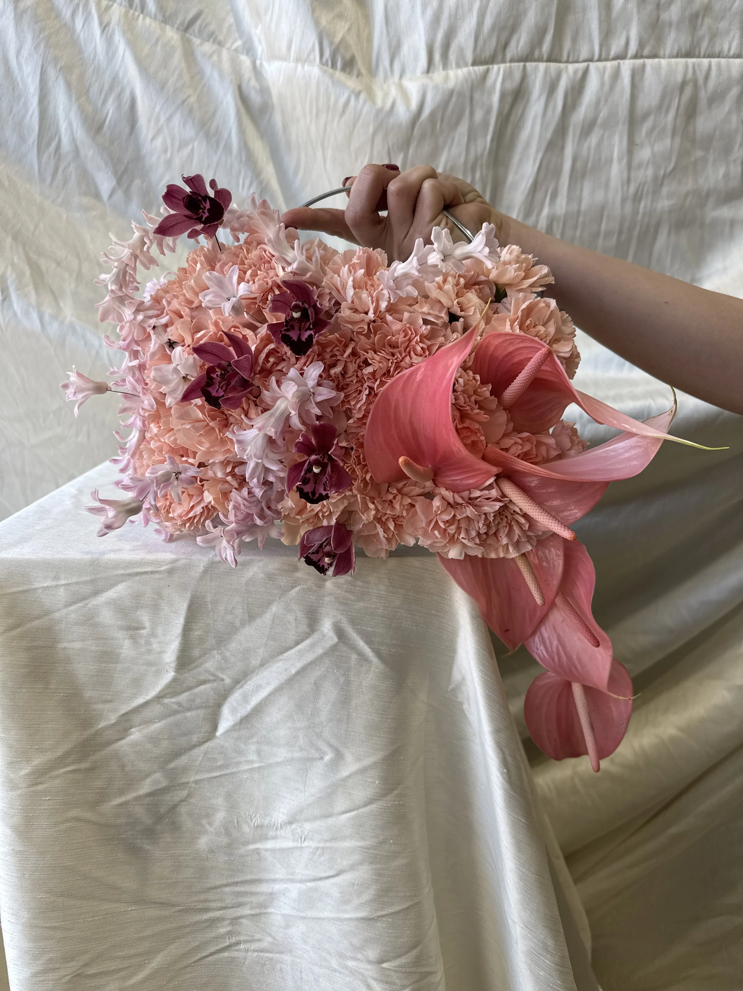 A hand holding a bouquet of pink, white, and purple flowers on a white fabric background.