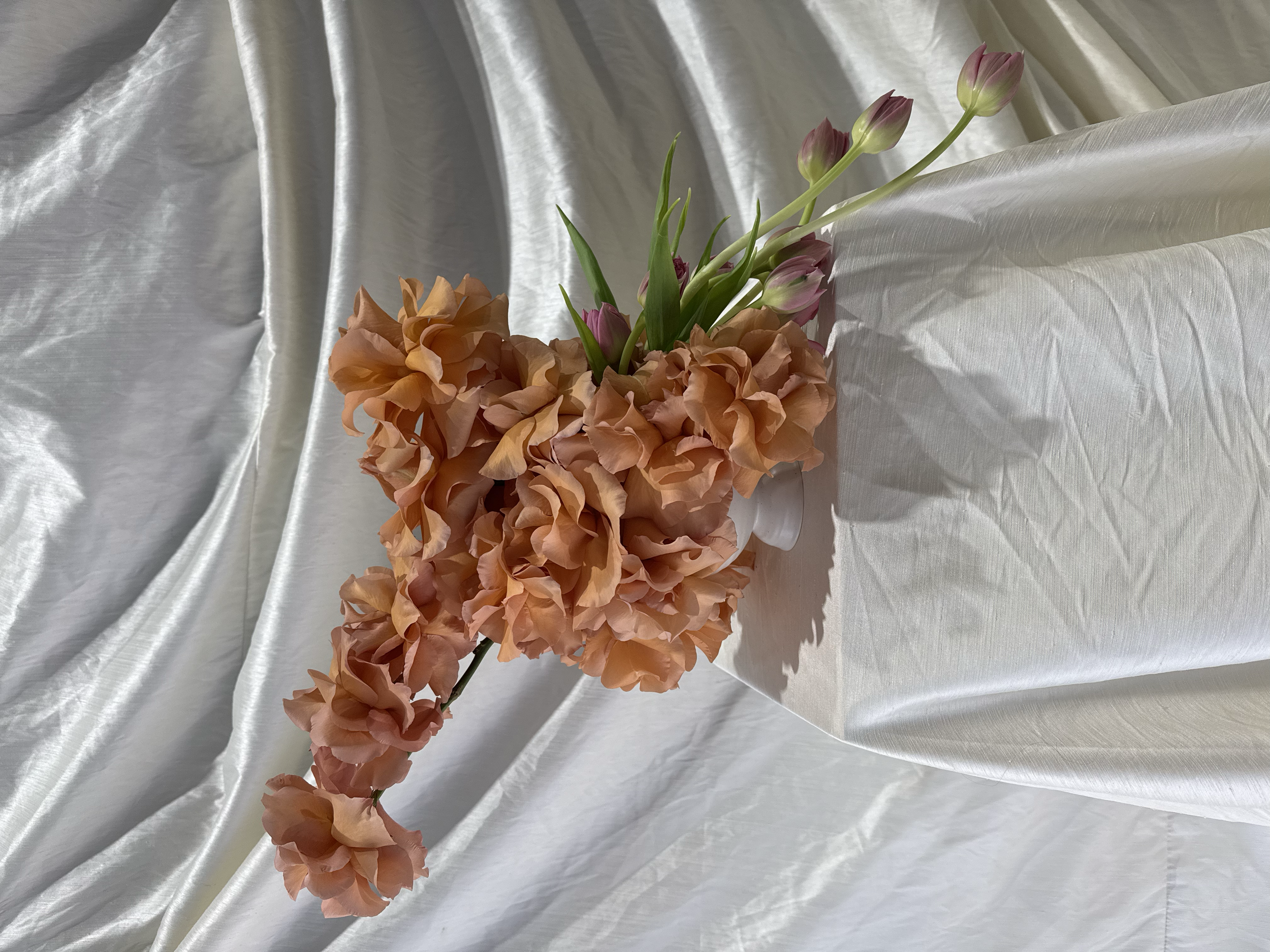 A bouquet of peach-colored and pink tulips resting on silver satin fabric.
