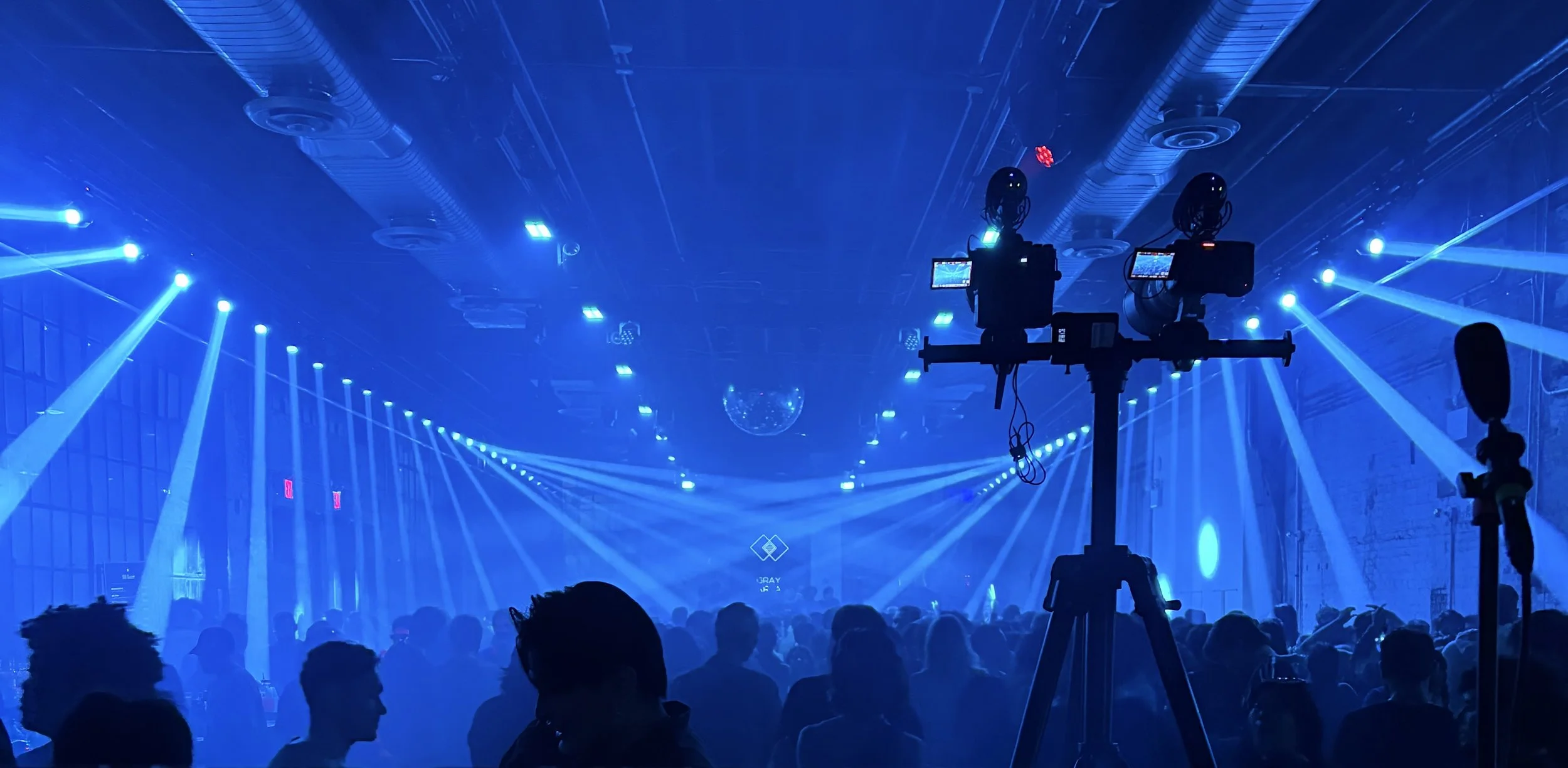 Espectáculo de luces en un evento con muchas personas y equipo de grabación o fotografía en primer plano en un ambiente oscuro con luz azul y láseres.