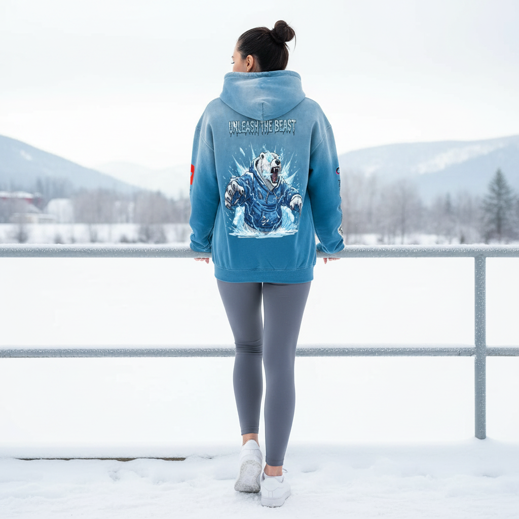 A woman in a blue hoodie with a polar bear graphic on the back stands on a snowy outdoor track, facing away. The hoodie features the text "Unleash the Beast." She is also wearing gray leggings and white sneakers, with a snow-covered landscape and dis