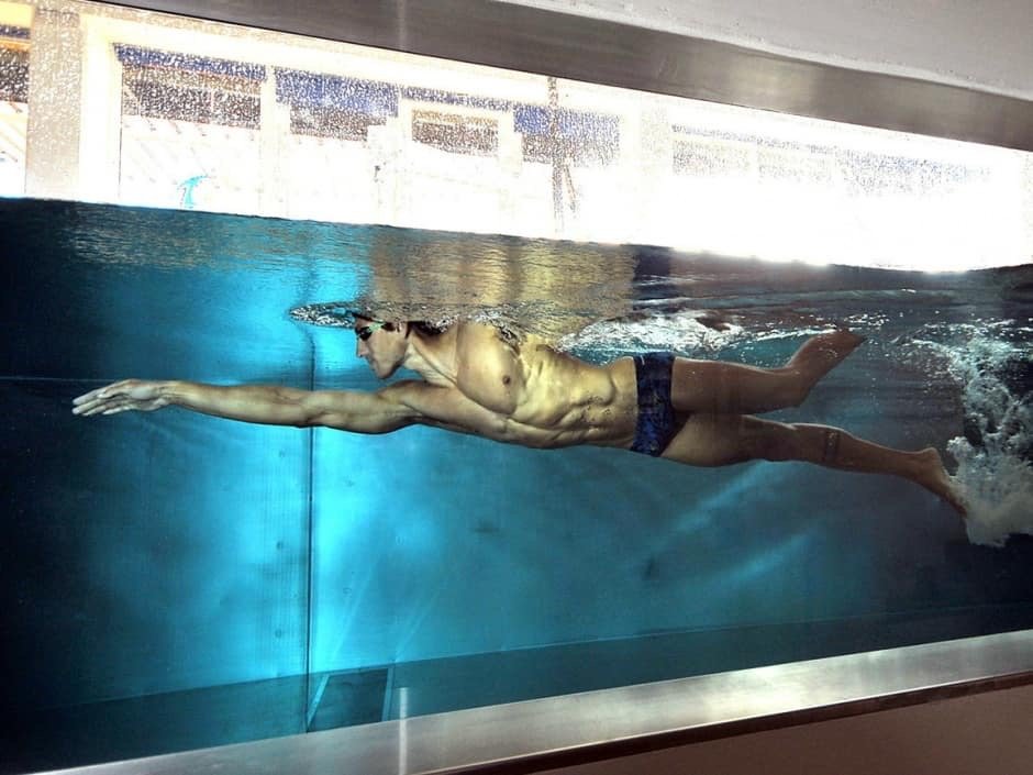 Mann schwimmt horizontal in einem Schwimmbecken, streckt die Arme nach vorne währenddessen