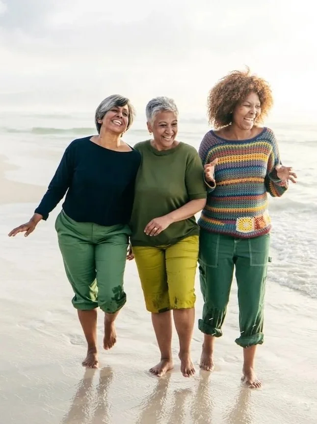 Three midlife women walking together along the beach, arms linked