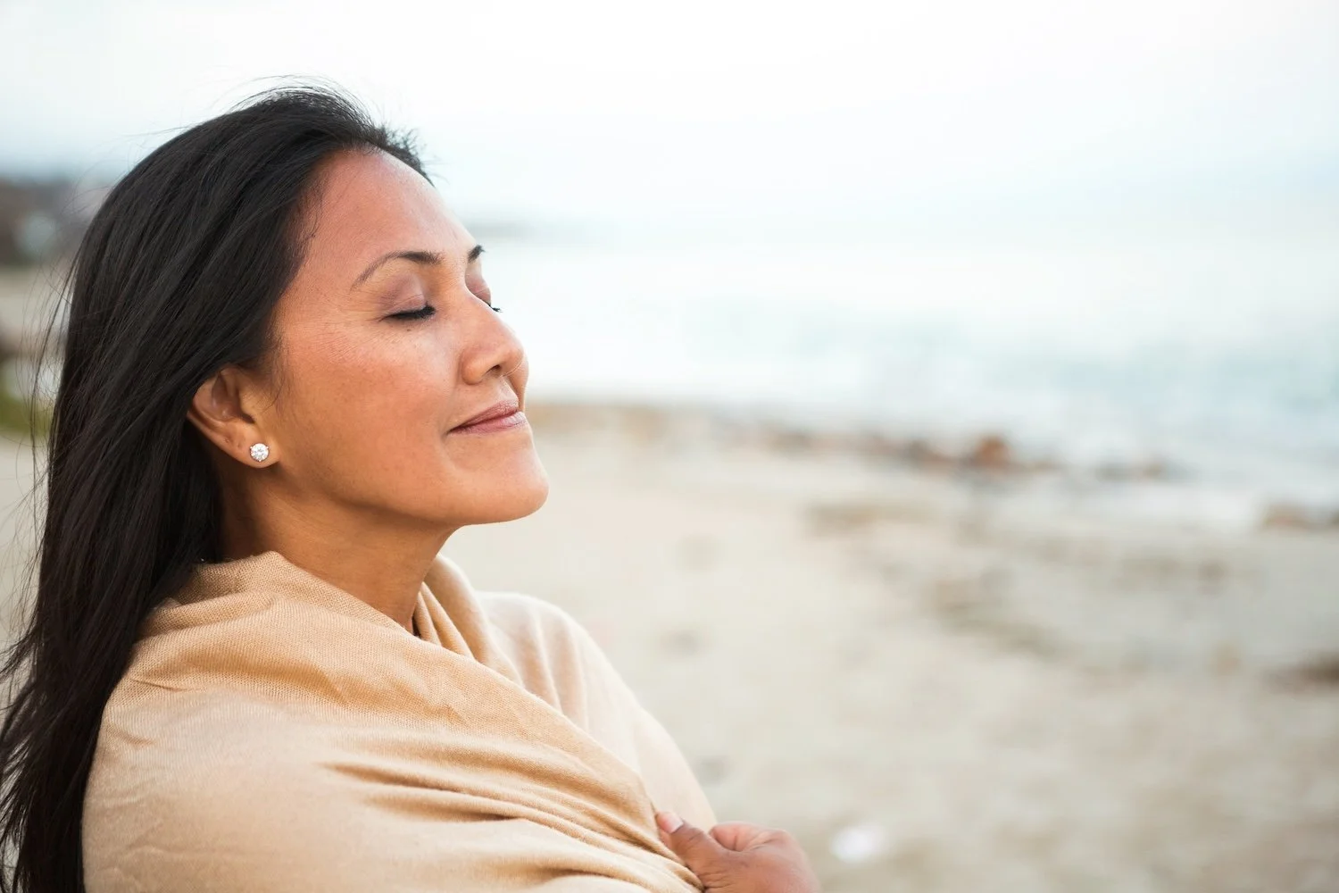 Woman with her eyes closed at the ocean, wrapped in a shawl