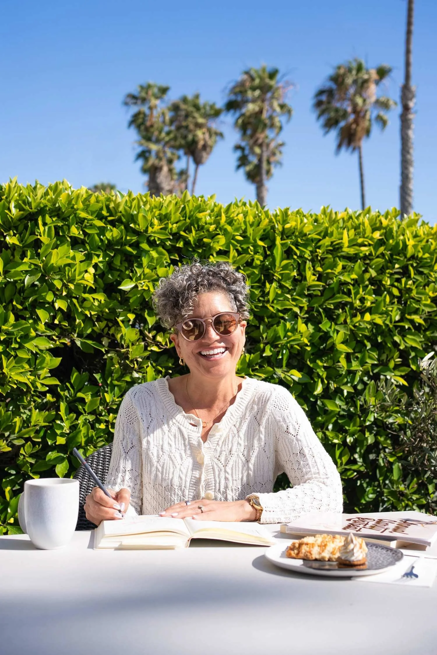Kerry Ann Rockquemore writing outdoors at a table, with palm trees in the background