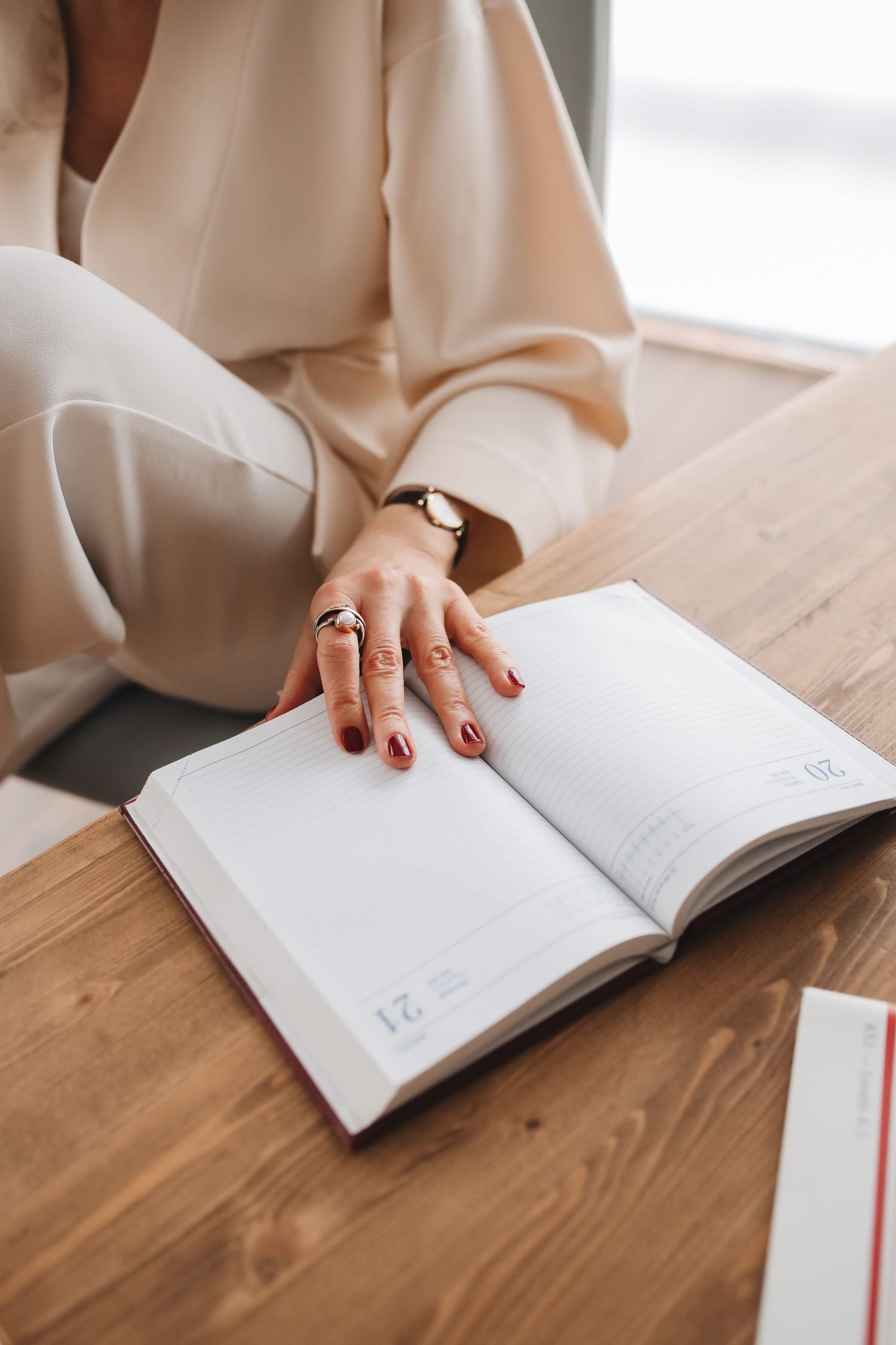 A woman's hand holding open a planner journal at a timber desk.