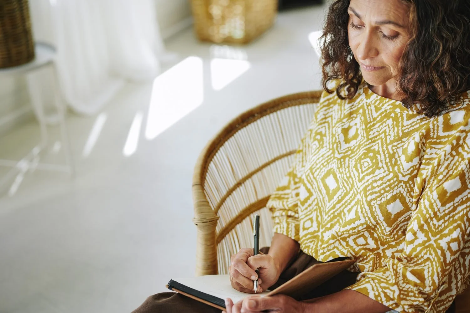 Woman journaling in a rattan chair, working through her Clarity Retreat workbook