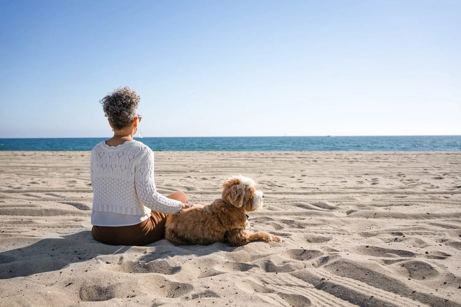 Kerry Ann sitting on the beach with her dog, looking out at the ocean