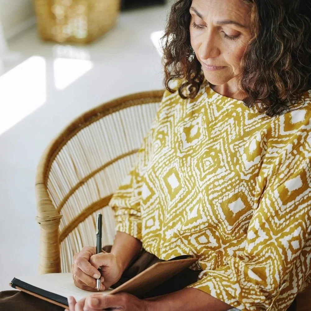 Woman journaling quietly in a rattan chair during a moment of private reflection