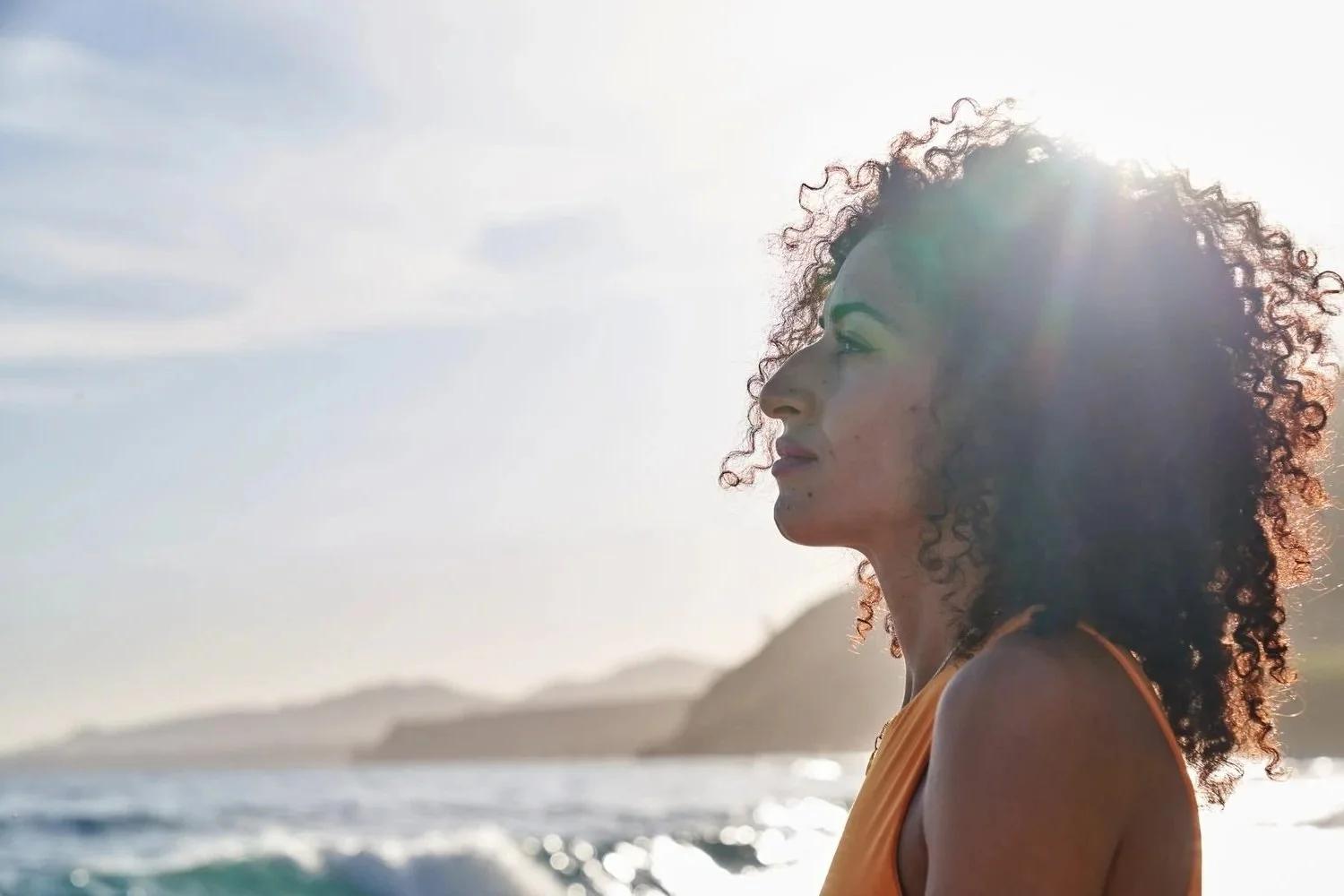Woman gazing toward the ocean during golden hour, reflecting on her next chapter in midlife