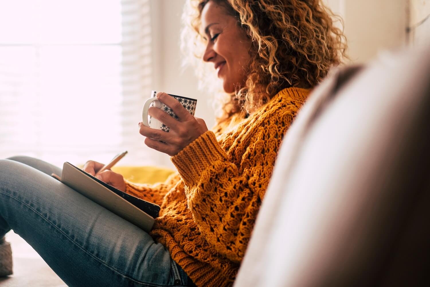 Woman relaxing on her couch with a warm drink, journaling during quiet reflection