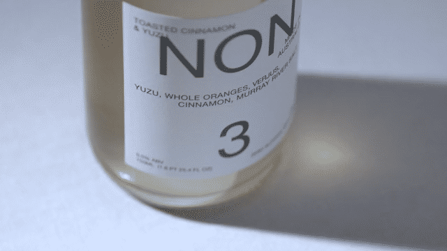 Close-up of a bottle label with the word 'NON' and flavor details like yuzu, oranges, cinnamon, and murray.