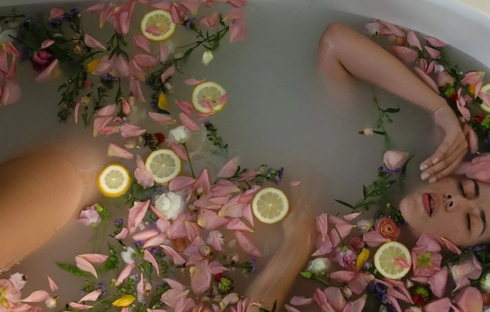 A woman relaxing in a bath surrounded by flower petals, lemon slices, and small flowers.