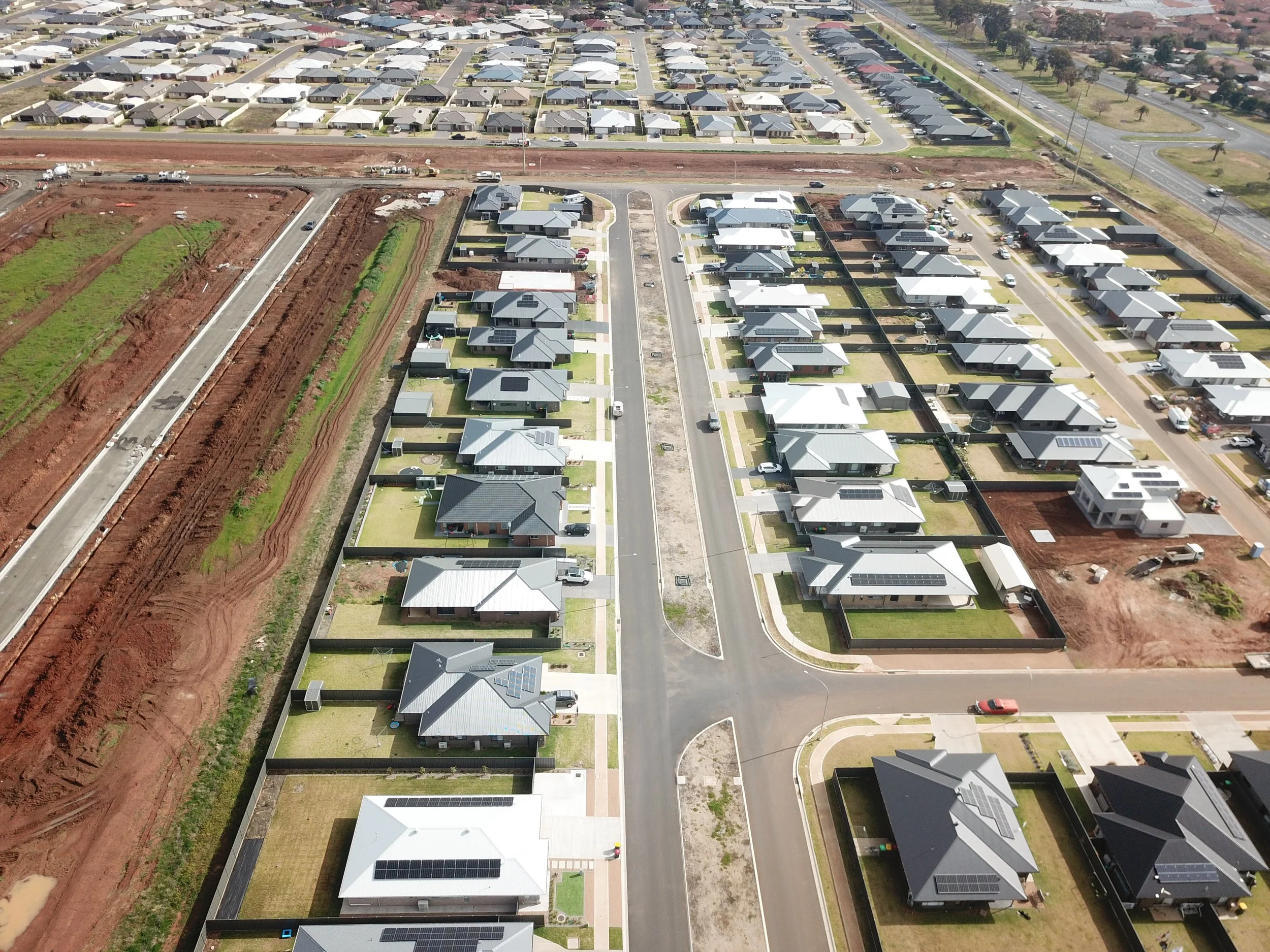 Aerial view of a residential neighborhood with houses, streets, and ongoing construction with red soil and gravel areas.
