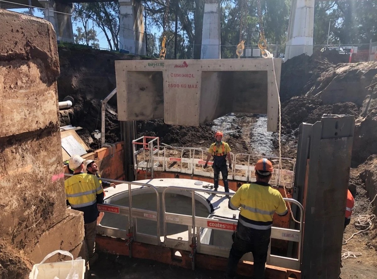 Construction workers standing around a large underground infrastructure, with a large concrete structure and excavation site in the background.