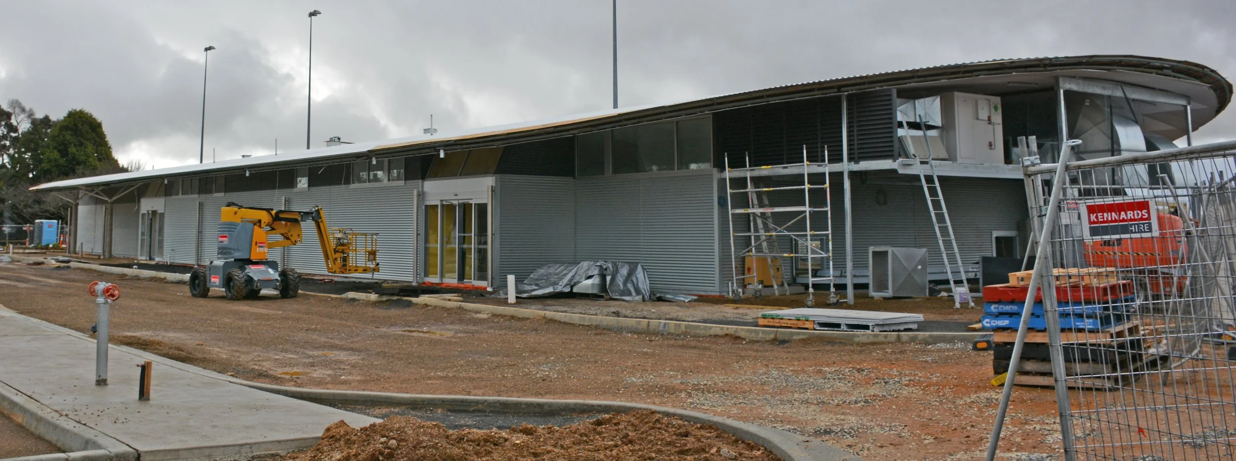 Construction site with a modern building under construction, including scaffolding and a lift, on a cloudy day.