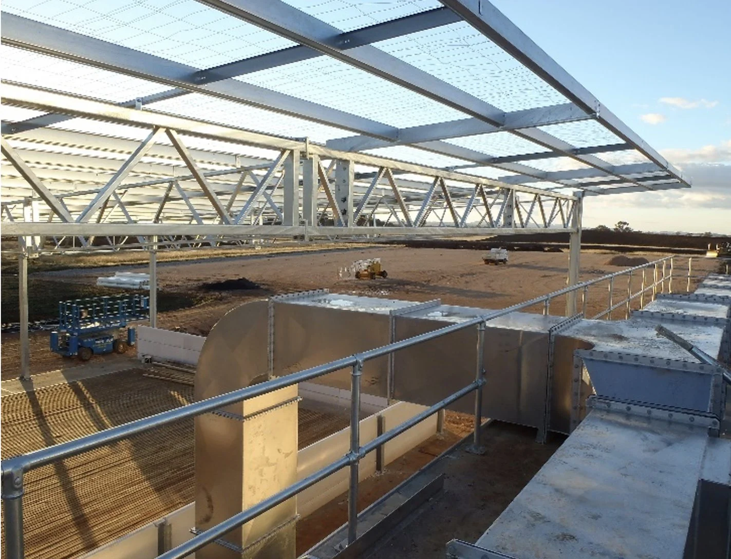 Construction site with metallic framework and solar panels on top, located on a dirt field during daytime.