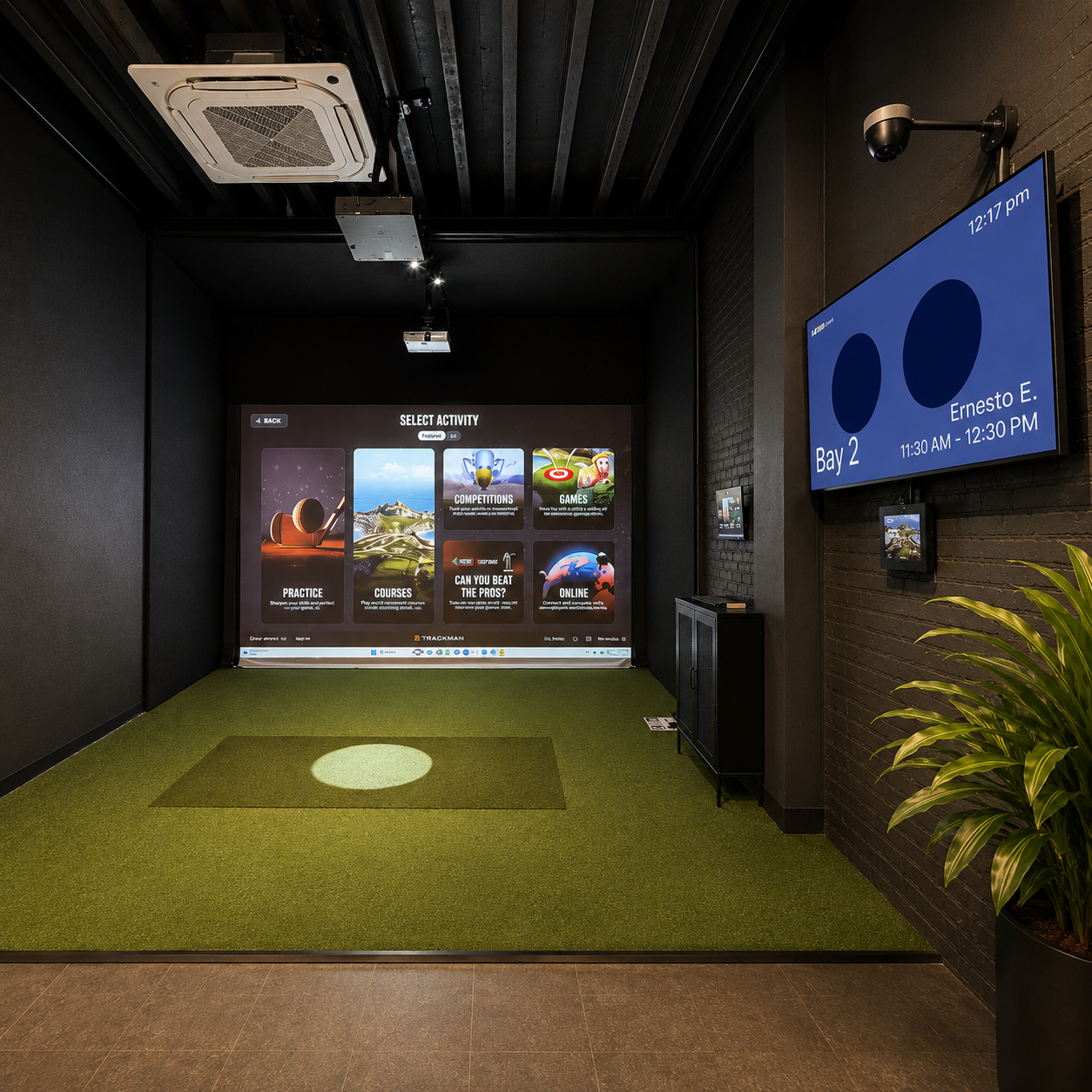 Indoor golf simulator room with a large screen displaying an activity selection menu, a green turf mat, a digital screen on the wall showing user information, and a potted plant in the corner.
