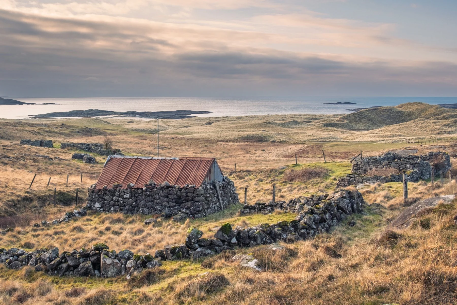 A derelict stone croft building with a rusting red corrugated iron/tin roof sitting behind the sand dunes of Sanna with the beach and see in the distance | Ardnamurchan Scotland | Steven Marshall Photography