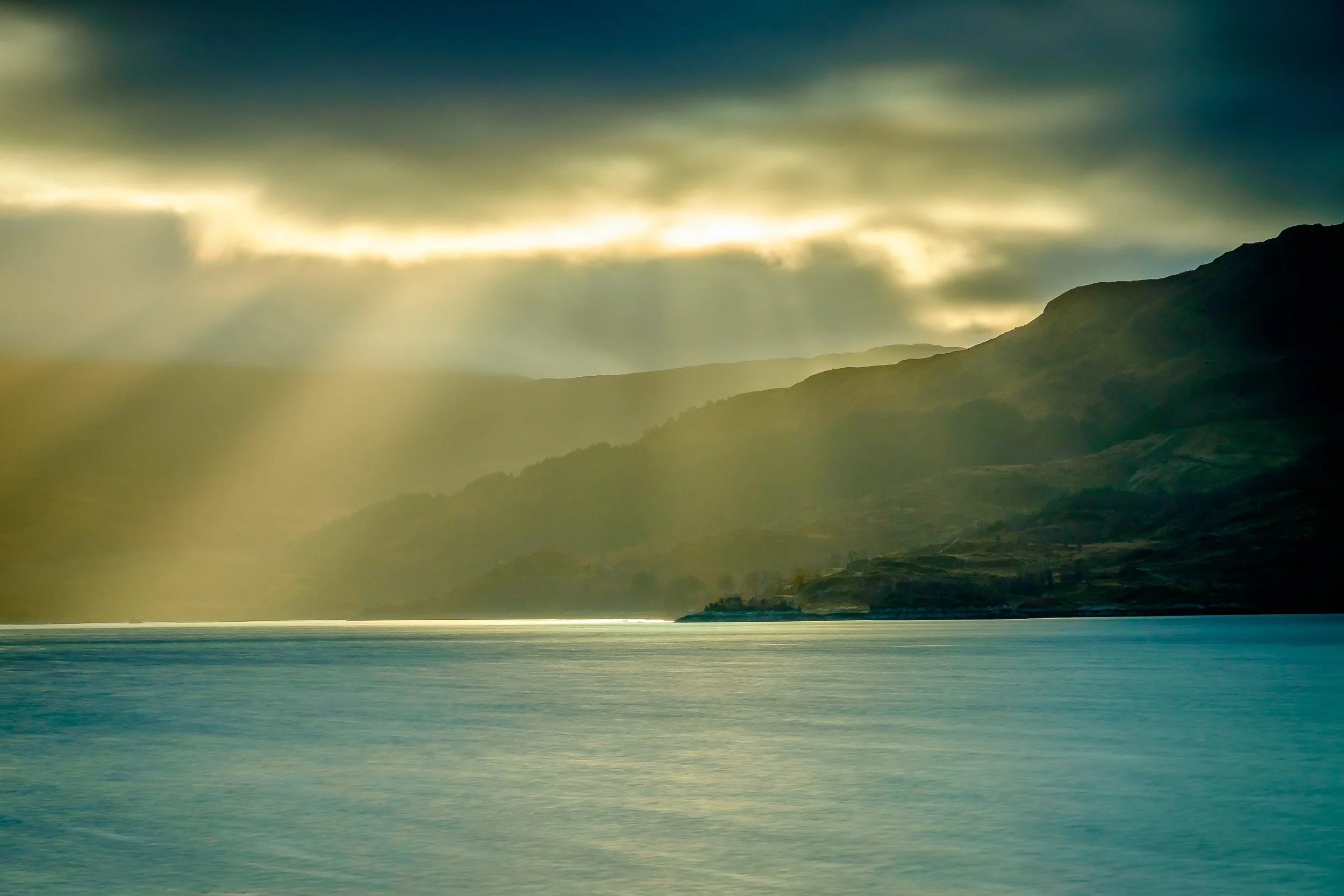 A landscape scene of the hills around Loch Sunart with cloudy sky and and sunlight breaking through clouds to light up the sea | Steven Marshall Photography