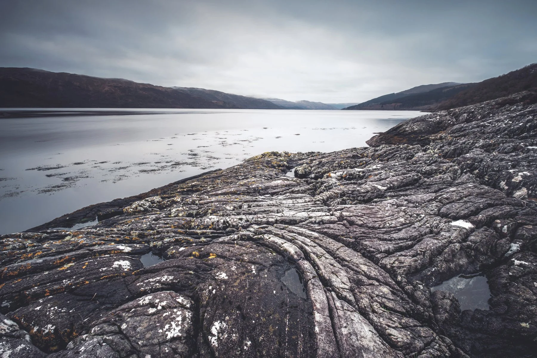 Dark rocks with curved grooves in them on the shore of Loch Sunart at Sàilean nan Cuileag | Sunart Scotland | Steven Marshall Photography