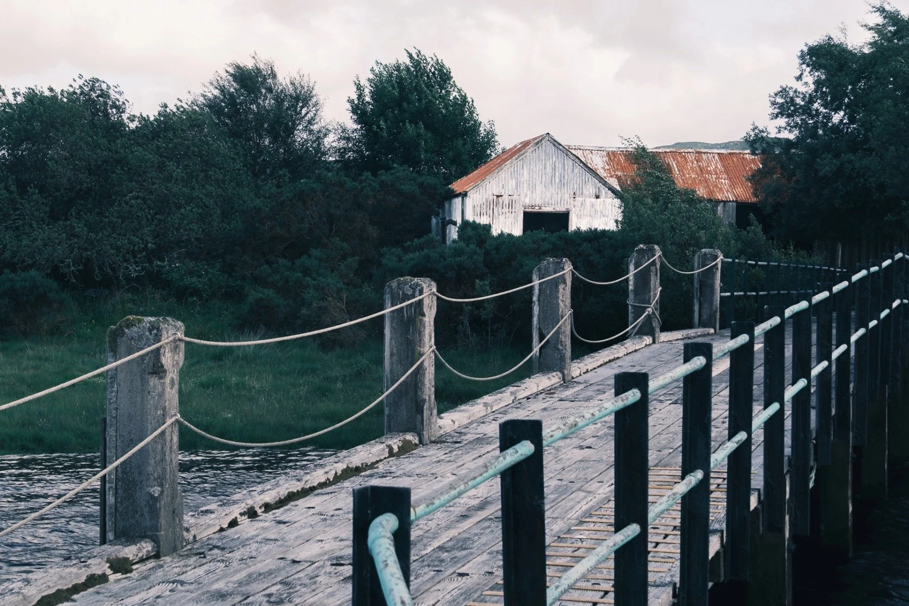 A wooden pier leading to a white walled, rusting red roofed and dilapidated and building | Acharacle Ardnamurchan Scotland | Steven Marshall Photography