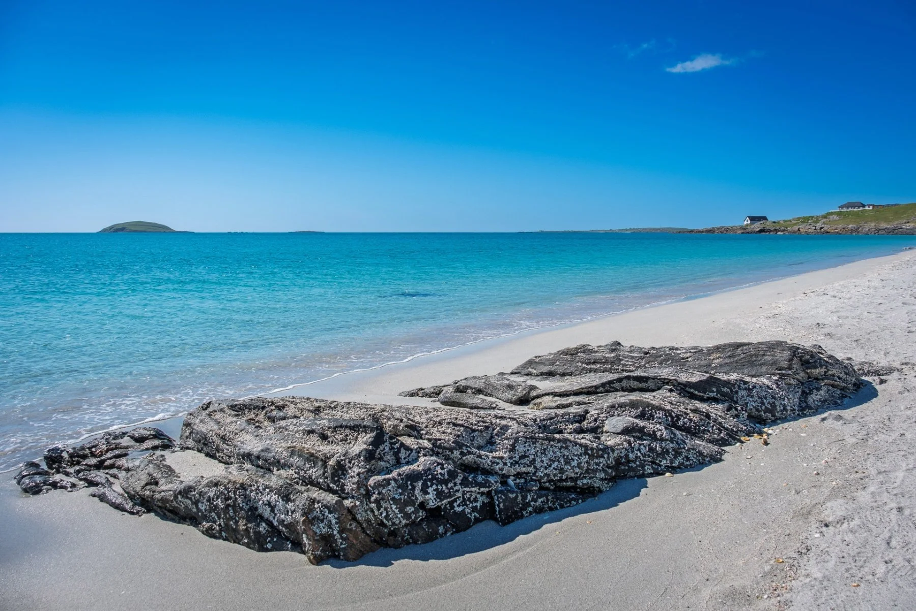 Waves lapping on the white sands of Coilleag a Phrionnsa, Eriskay, known as the Prince’s Beach with a large boulder in the foreground | Outer Hebrides Scotland | Steven Marshall Photography