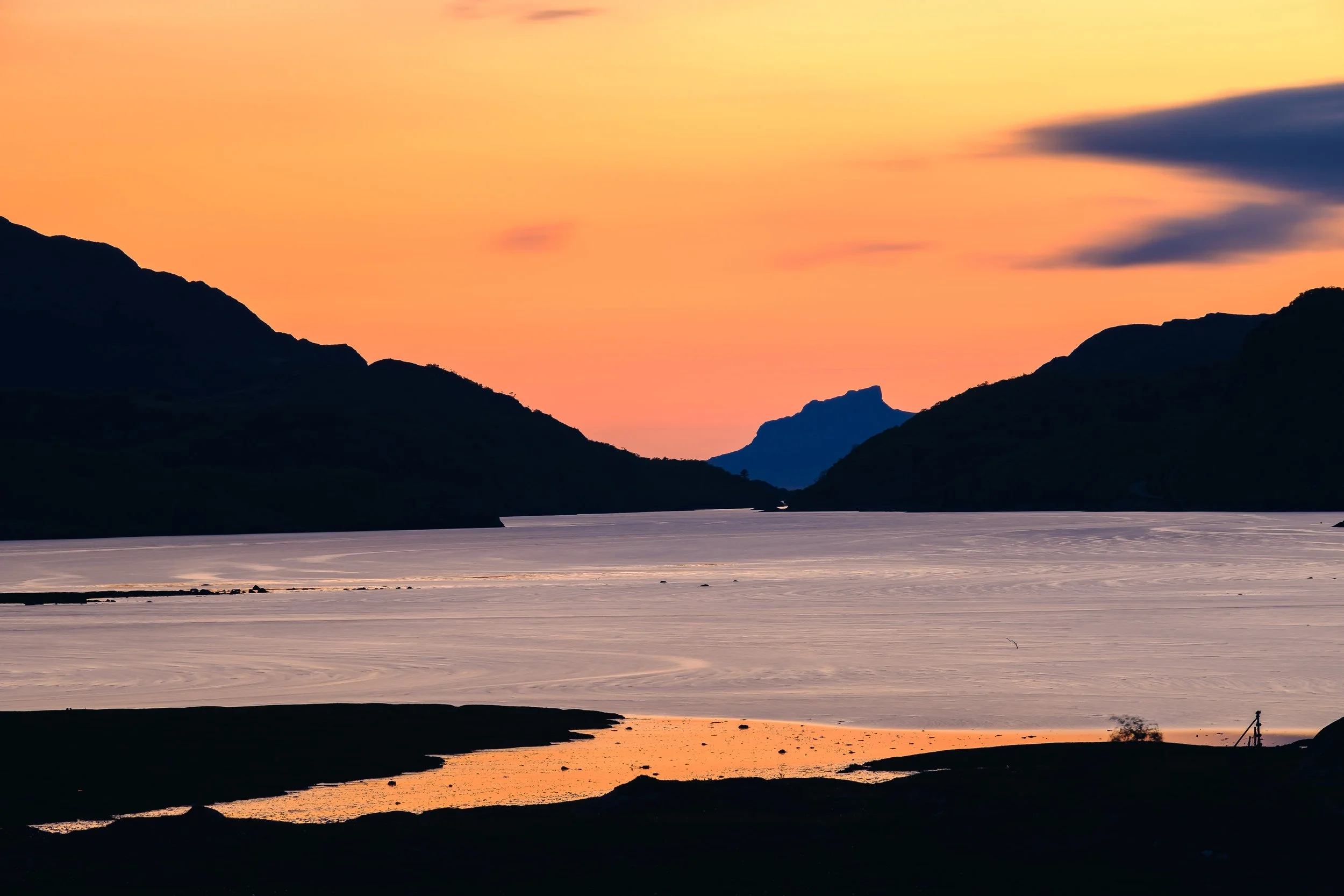 A scenic view of a sunset over Loch Moidart  mountains and a reflective body of water, with a pink and orange sky and dark silhouetted mountains in the foreground | Steven Marshall Photography