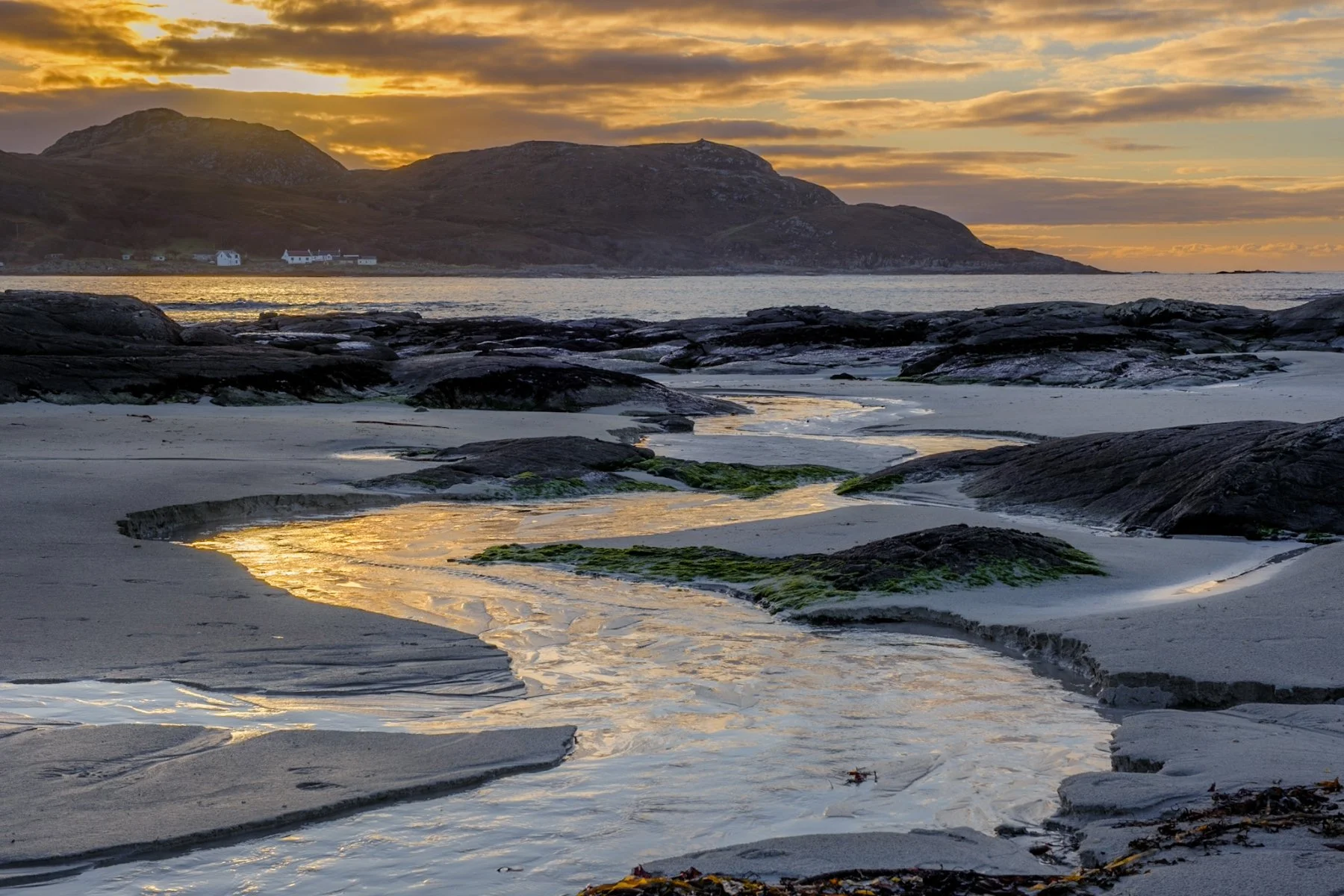 Sunset over a stream running through the sand at Sanna Beach with gold light illuminating the clouds in the sky above Portuairk | Ardnamurchan Scotland | Steven Marshall Photography