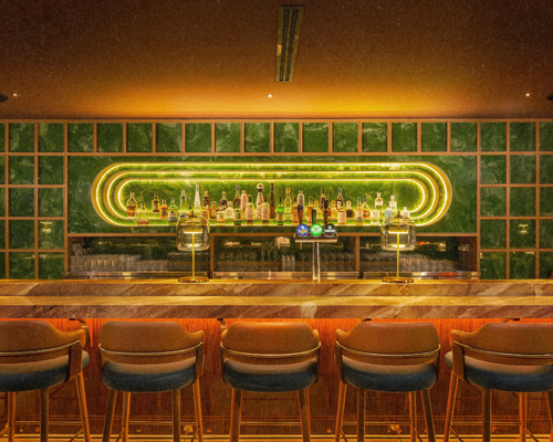 Interior of a modern restaurant/bar with a large potted plant in the center, surrounded by seating areas, a bar with alcohol bottles in the background, and decorative lighting.